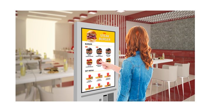 A woman is touching a kiosk to select a hamburger from the menu.